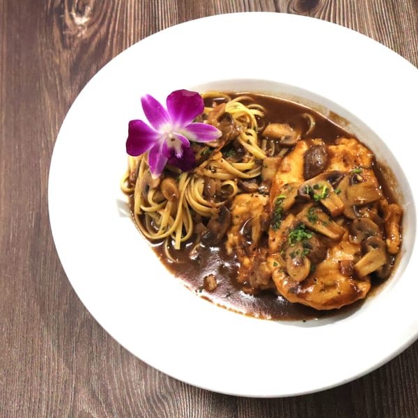 Chicken and mushroom pasta with a purple orchid garnish on a white plate.