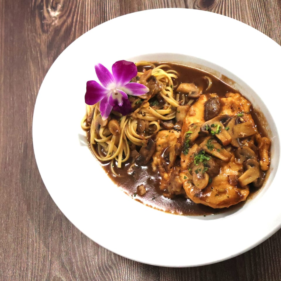 Chicken and mushroom pasta with a purple orchid garnish on a white plate.