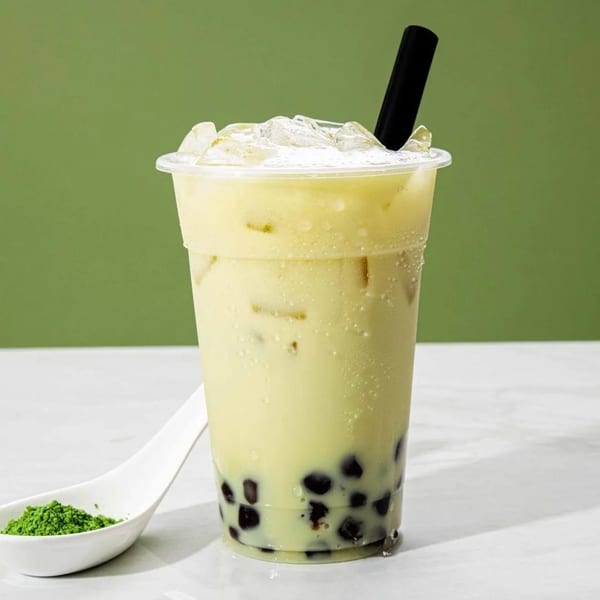 Iced matcha bubble tea with tapioca pearls and a spoon of matcha powder.