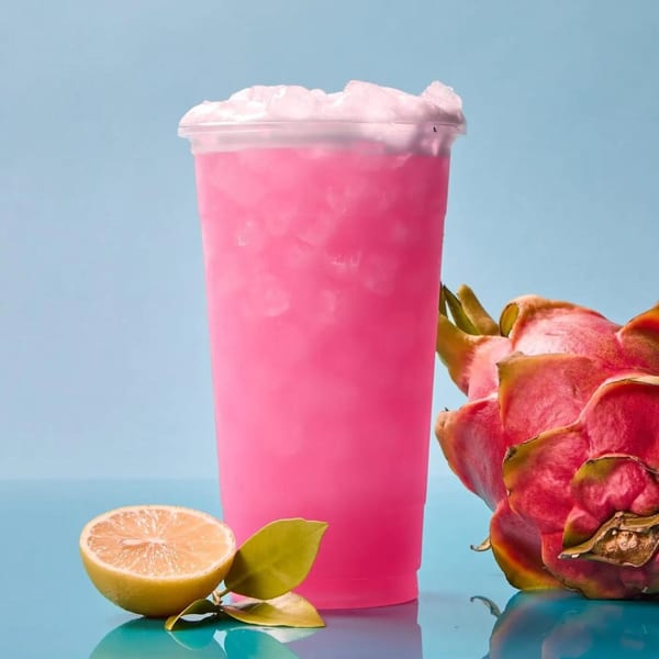 Pink iced drink with dragon fruit and a sliced lime on a blue background.