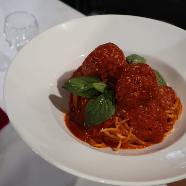 Spaghetti with two large meatballs, rich red sauce, fresh basil, and grated cheese in a white bowl.